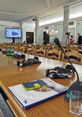 stoły konferencyjne, na nich mikrofony i słuchawki, w tle tablica multimedialna