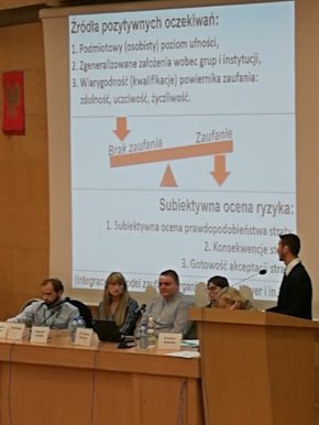 zdjęcie z konferencji, paneliści usadzeni przy stole, w tle prezentacja jednego z nich